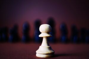 A white wooden chess piece facing black ones.