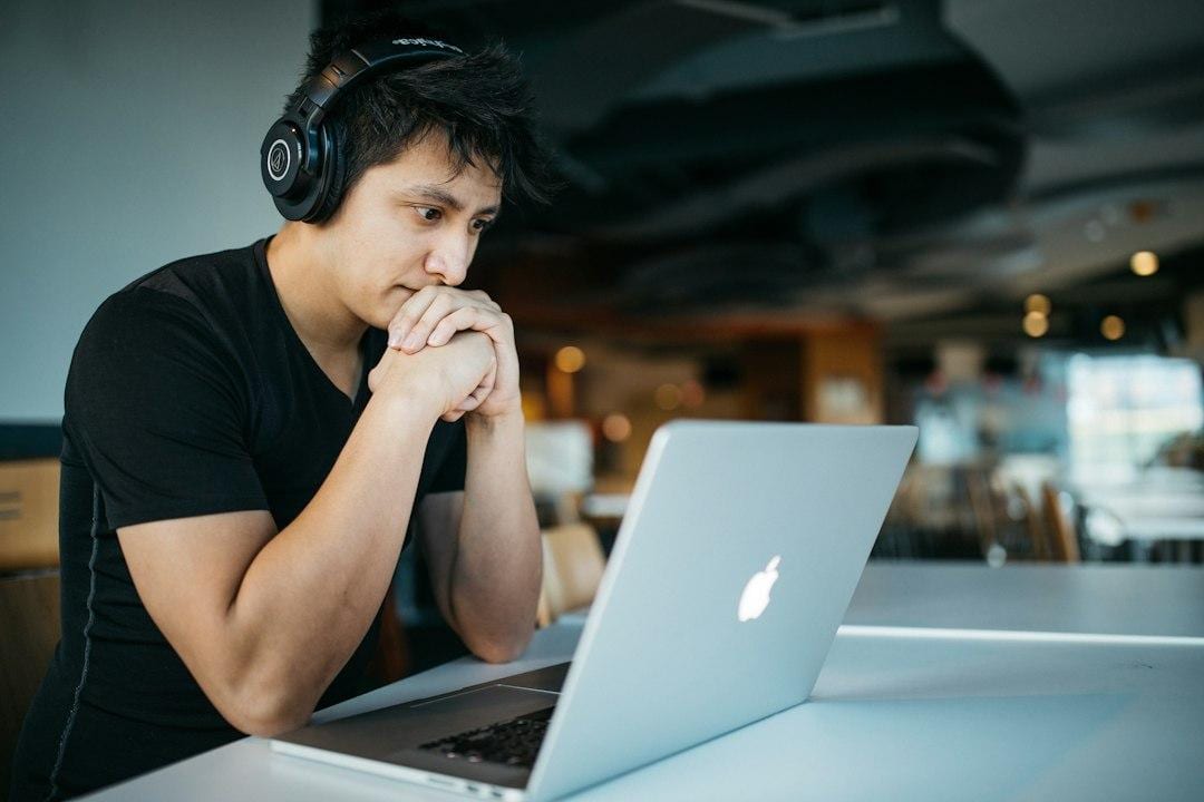 Man wearing headphones while sitting on a chair in front of a MacBook