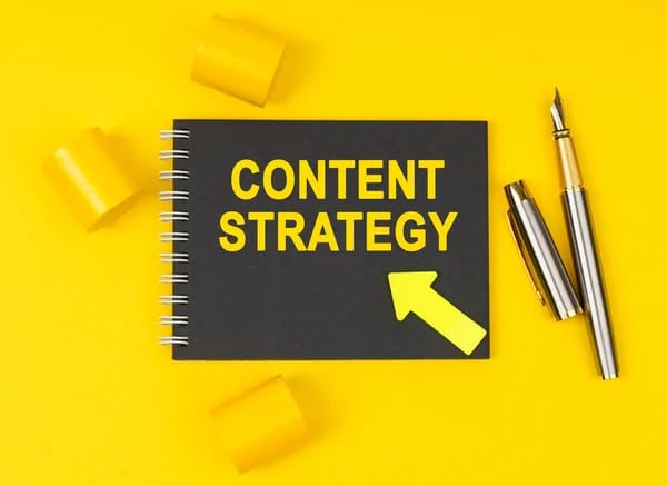 Black notebook reading Content Strategy on a yellow desk next to a fountain pen