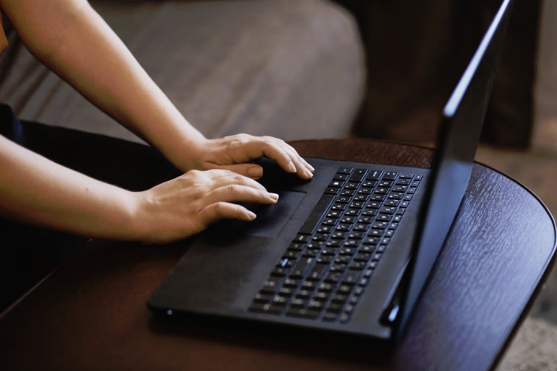 Hands typing on a black laptop on a round wooden table