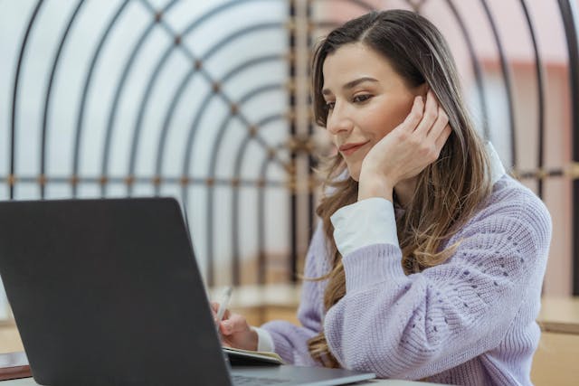 A woman in a purple sweater looking at her laptop